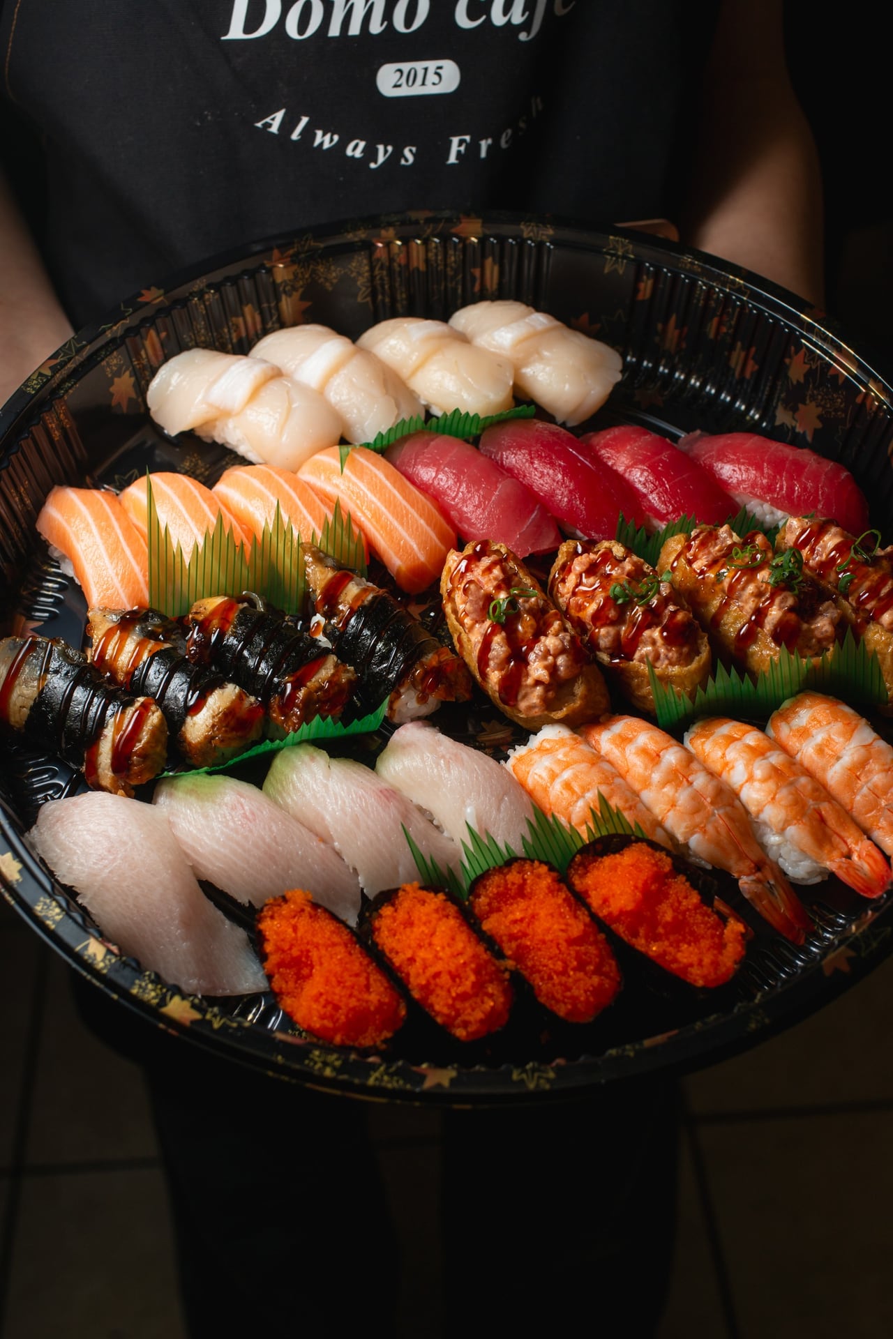 A Domo Cafe staff member holding a round nigiri platter with salmon, ahi, hamachi, ebi and ikura